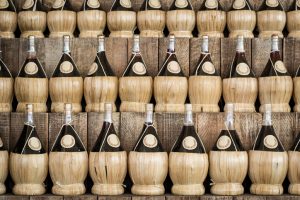 Três fileiras de garrafas de chianti tradicional com fundo de palah