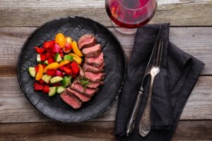 Mesa posta com prato de churrasco e legumes grelhados, e taça com vinho tinto.